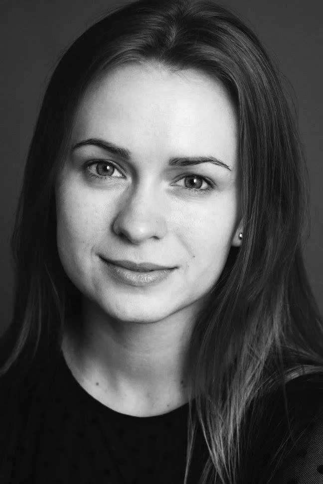 Black and white headshot of Krystyna with long straight hair, smiling softly