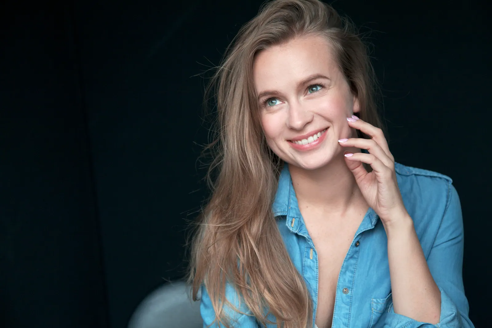 Krystyna Vyzhu in a denim shirt, smiling, against a dark blue studio backdrop