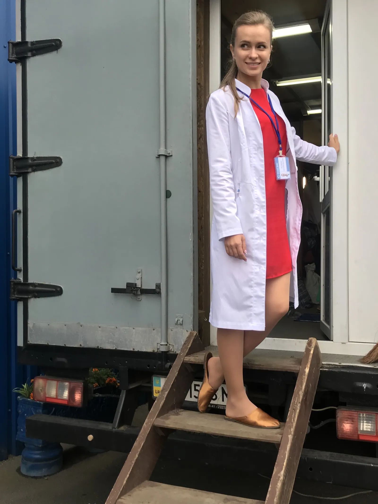 Krystyna in costume, a white doctor’s coat, on the steps of a production trailer