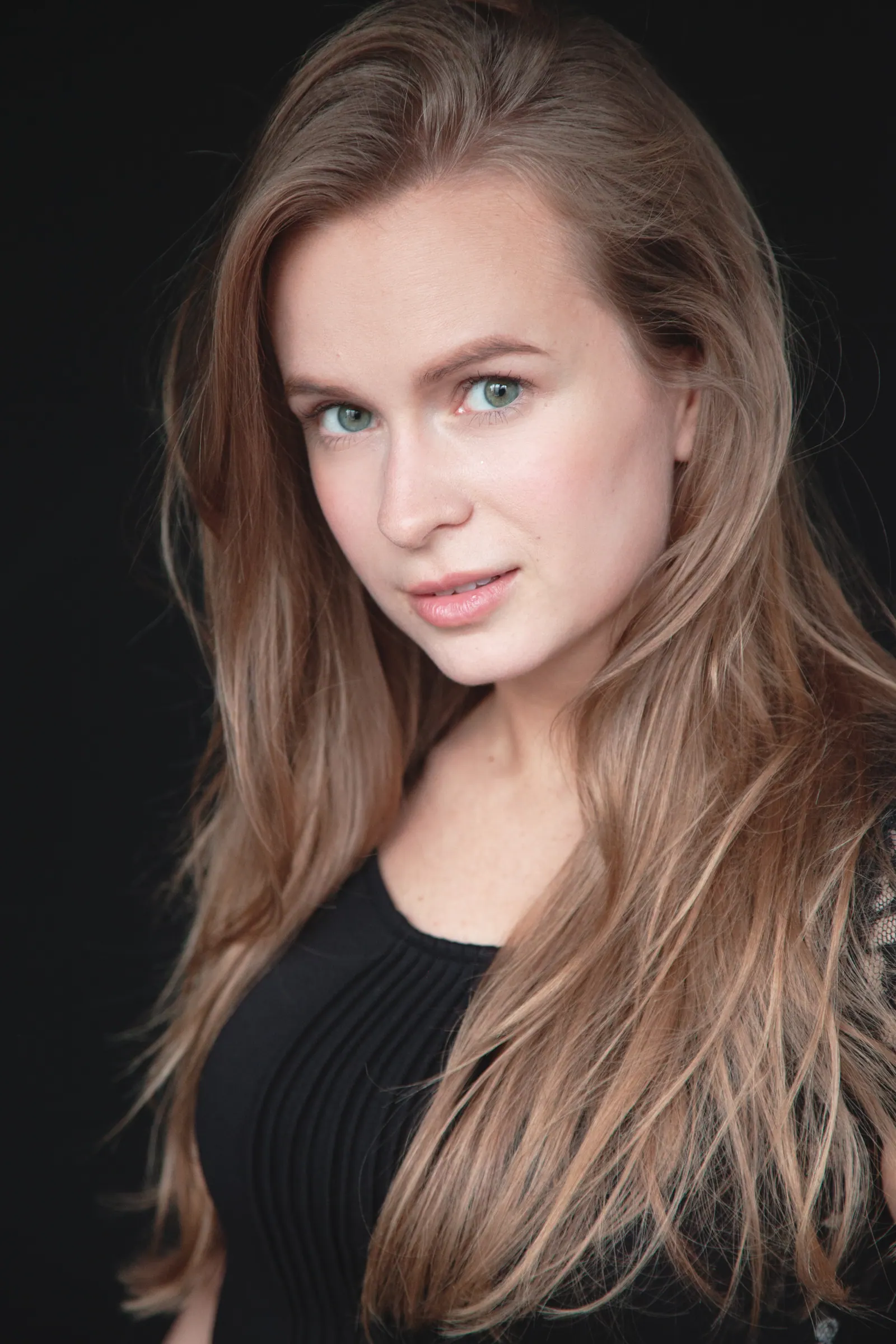 Krystyna in a black top against a dark backdrop, hair over one shoulder