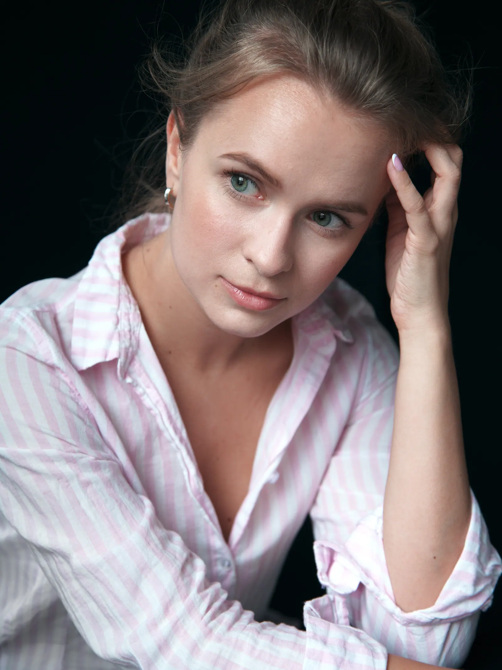 Krystyna in a pink striped shirt, hand at her temple