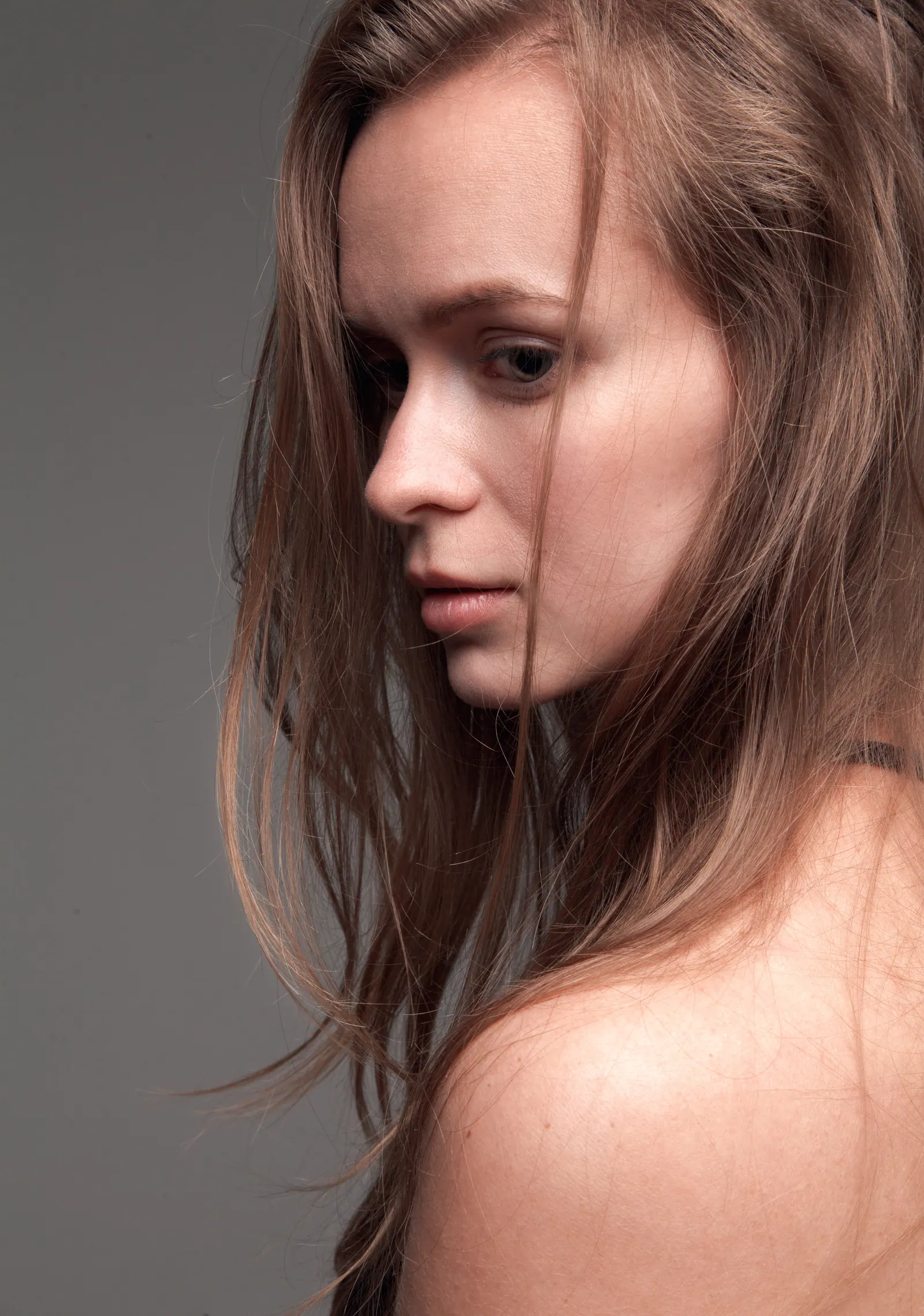 Krystyna looking down over a bare shoulder against a grey backdrop